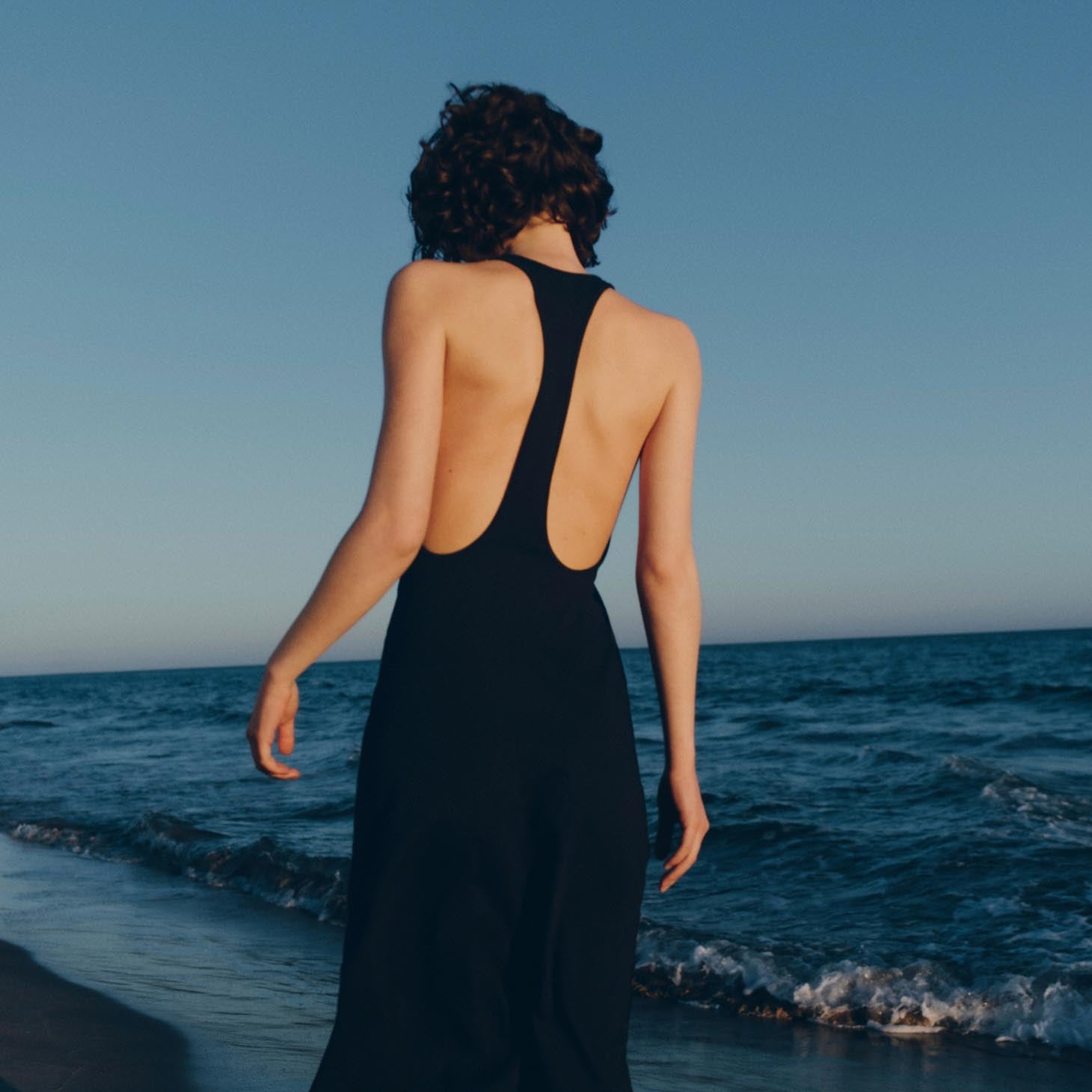 The back of a woman on a beach in a black racerback dress