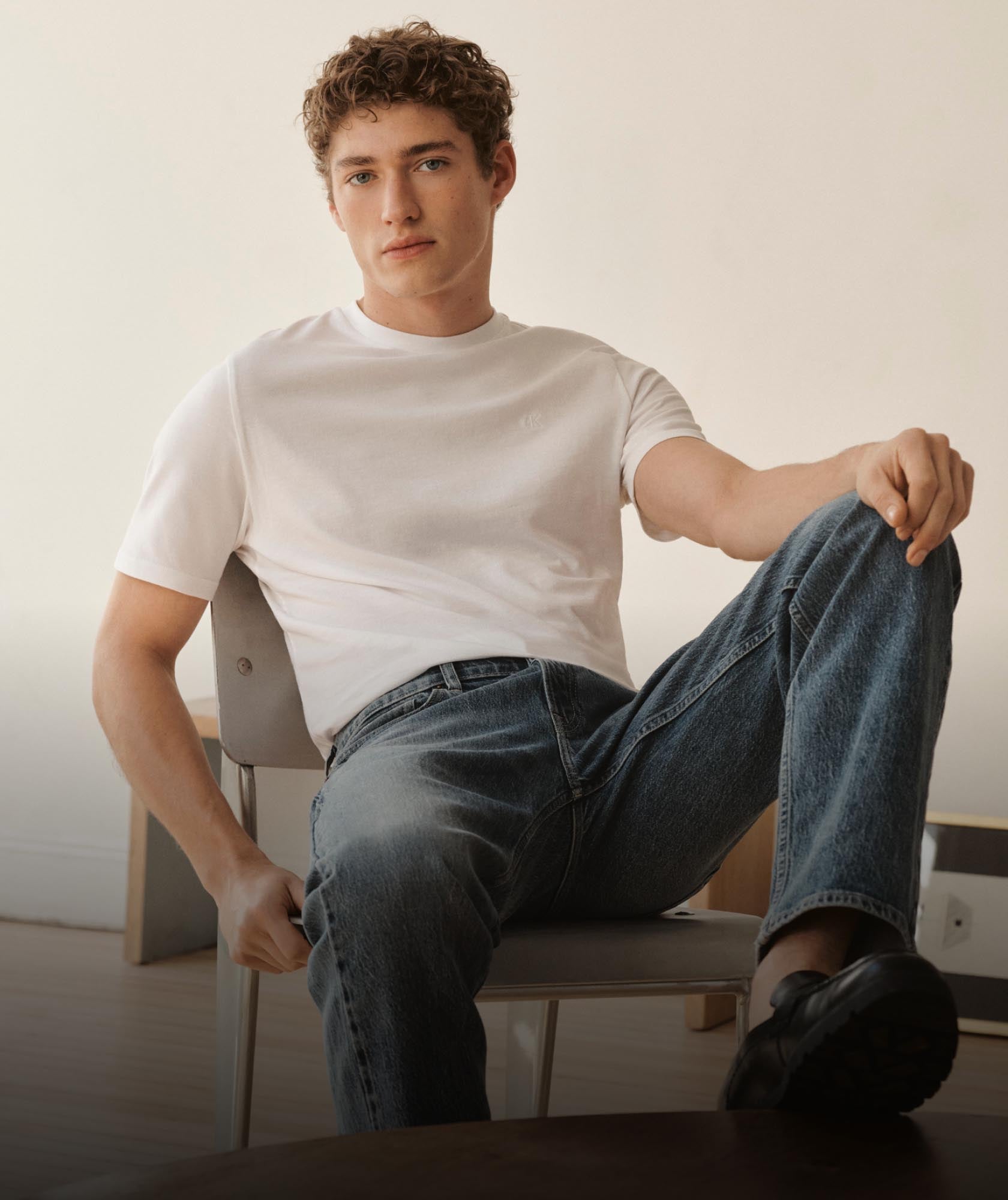 Man sitting in a chair with his leg up wearing medium wash denim jeans