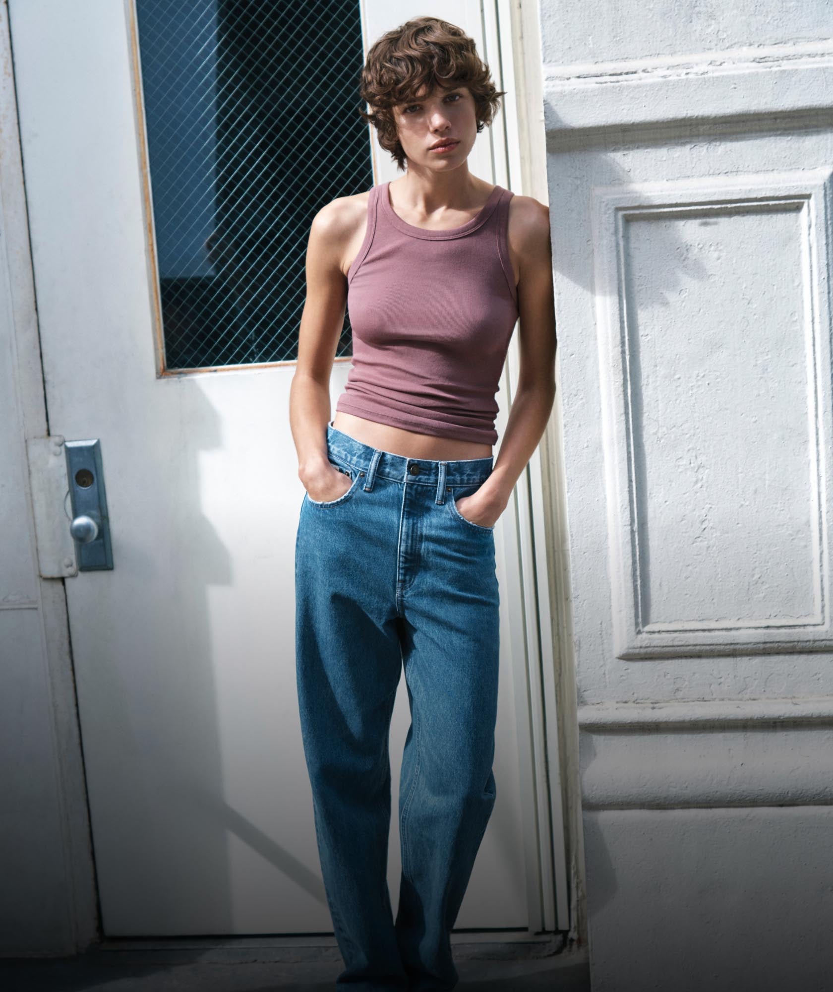 Woman posing with her arms raised wearing a white t-shirt and light blue relaxed denim jeans