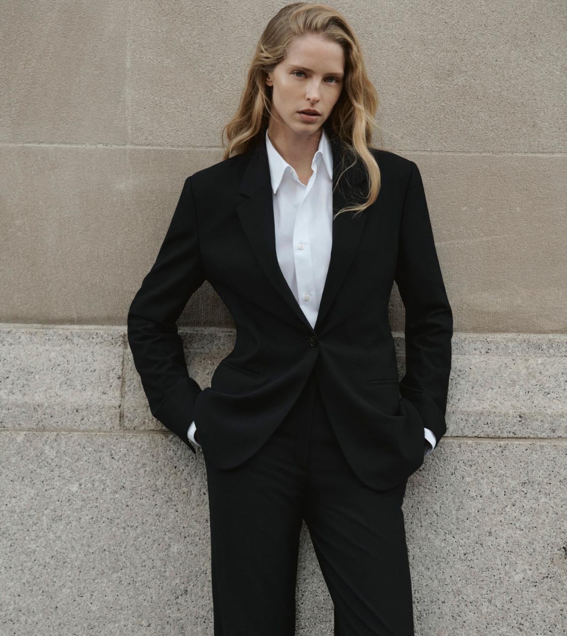 Woman posing with her hands in her pockets wearing a tailored black blazer and tailored white shirt