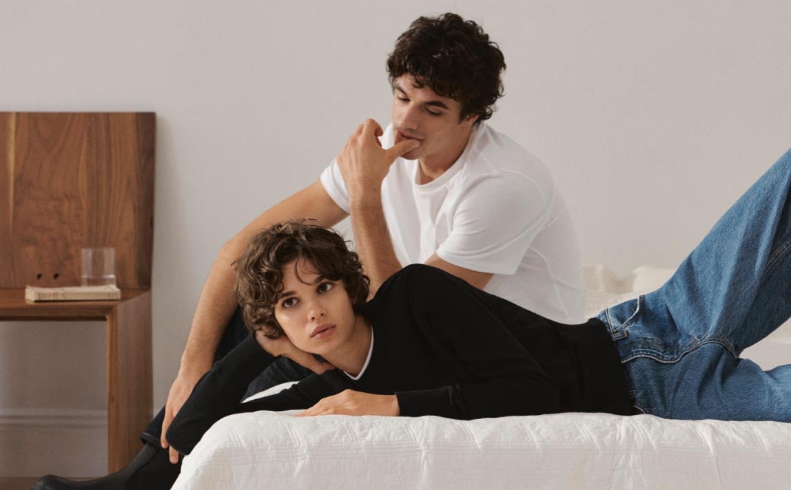 Man and a woman lying on a bed wearing casual Calvin Klein Essentials apparel styles