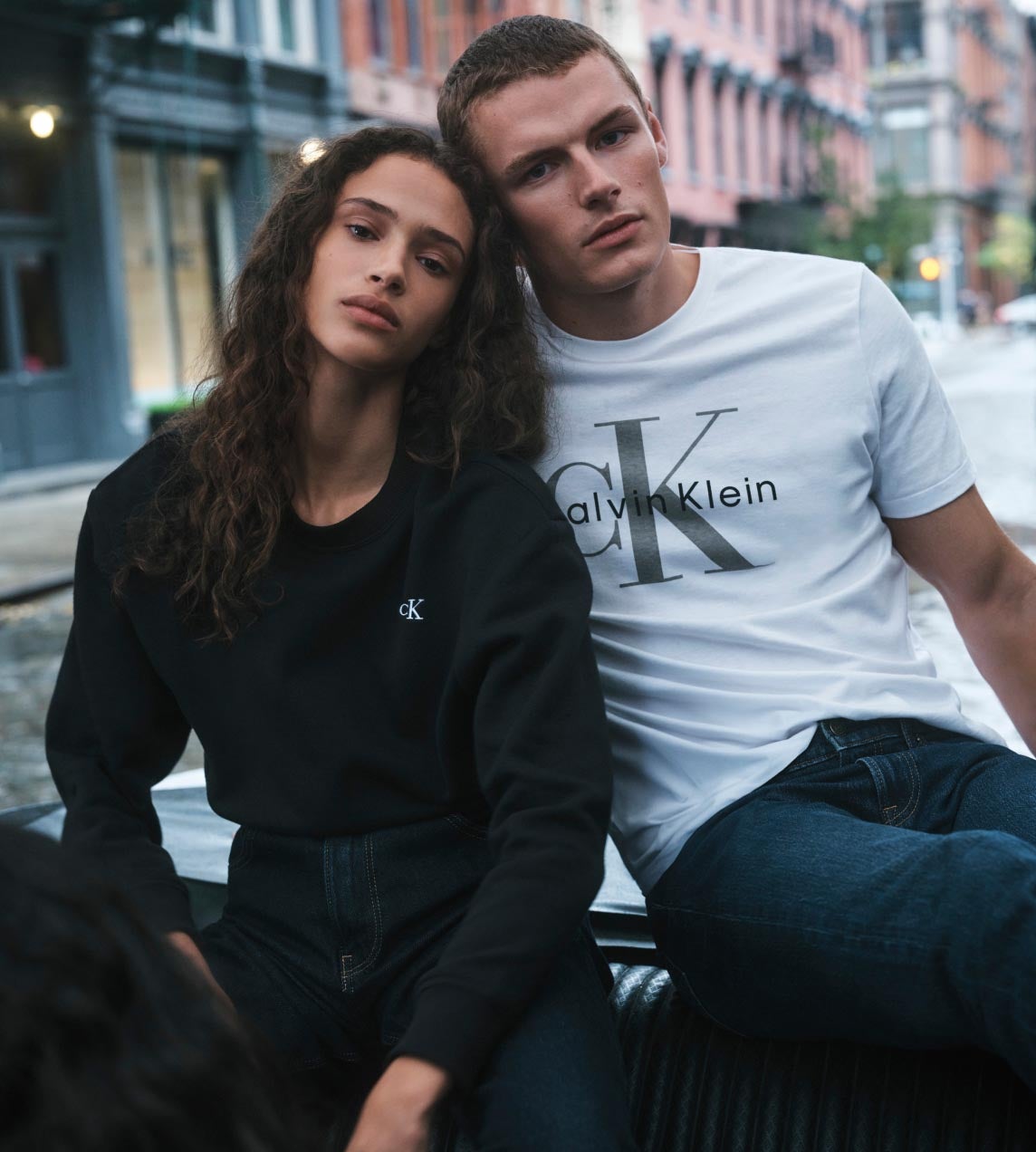 A man and a woman posing in a car wearing CK logo tees and sweatshirts