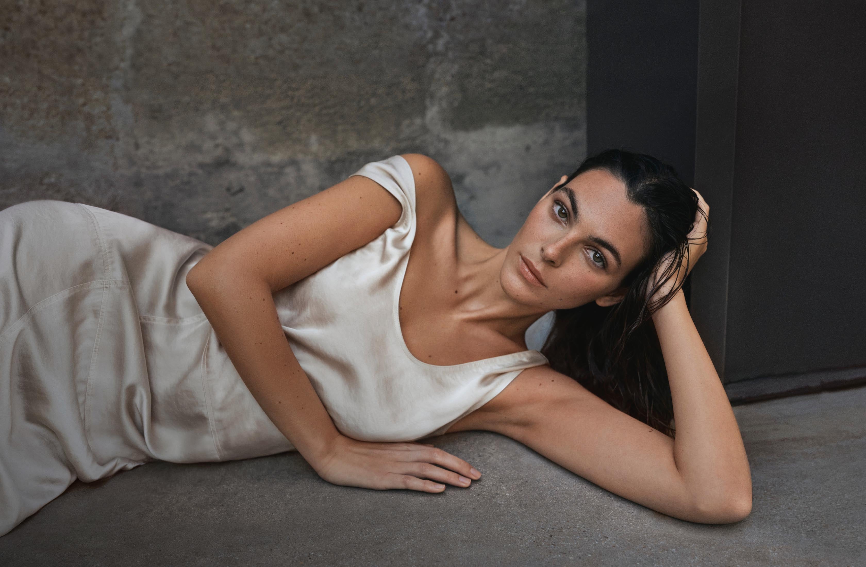 A model posing laying down on her side wearing a white satin maxi dress
