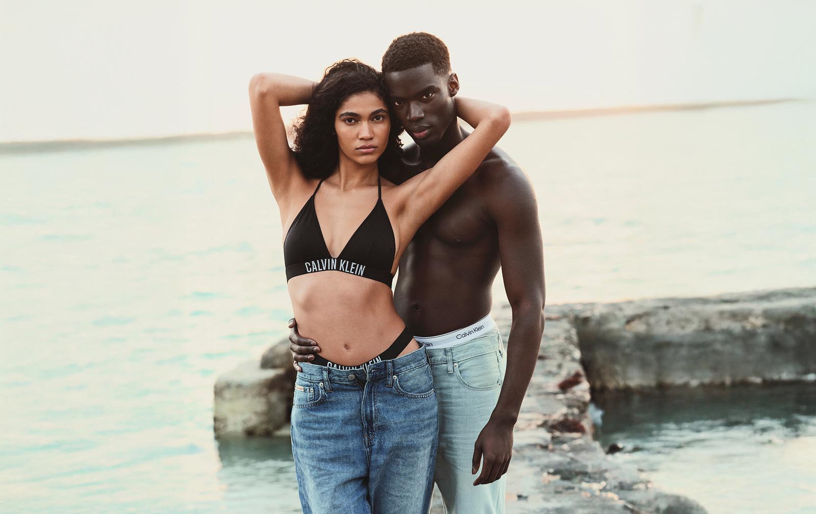 Color image of one model wearing Calvin Klein bikini top and bottom with jeans with another model wearing jeans.