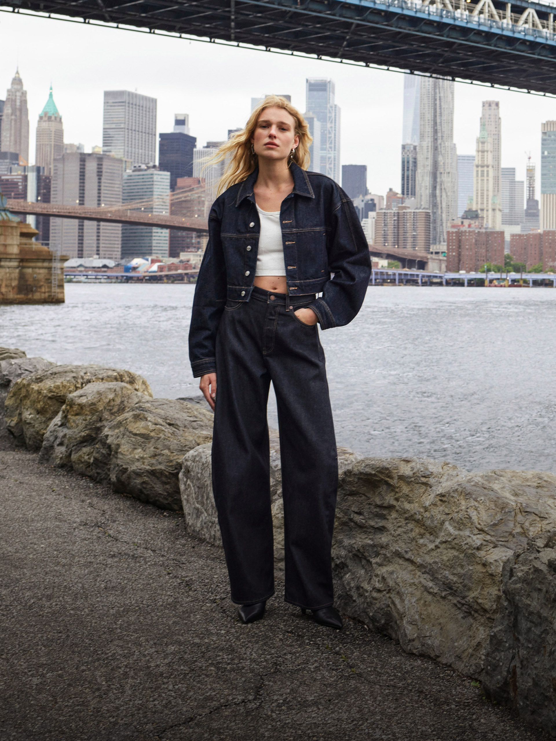 Model wearing a denim ensemble with white tank top and the Brooklyn Bridge in the background.