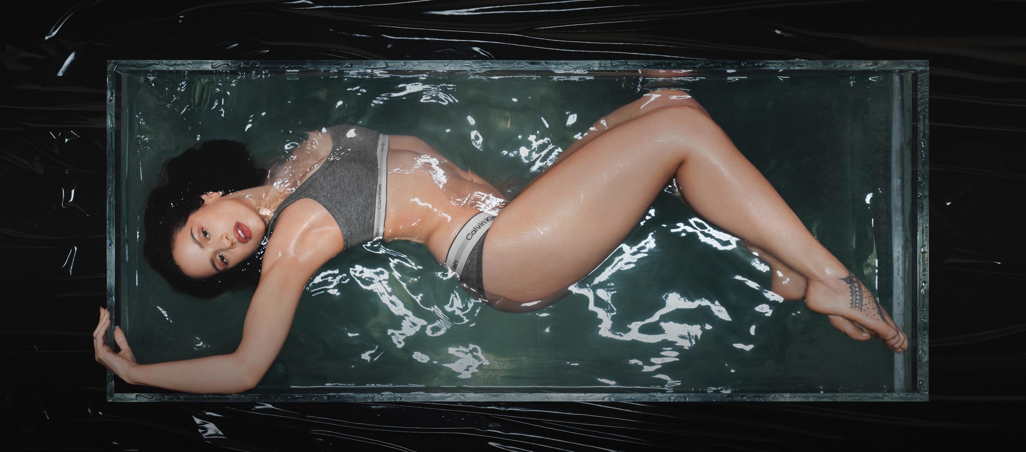 Rosalia laying down partially submerged in a water tank wearing grey Calvin Klein Heritage Cotton underwear.