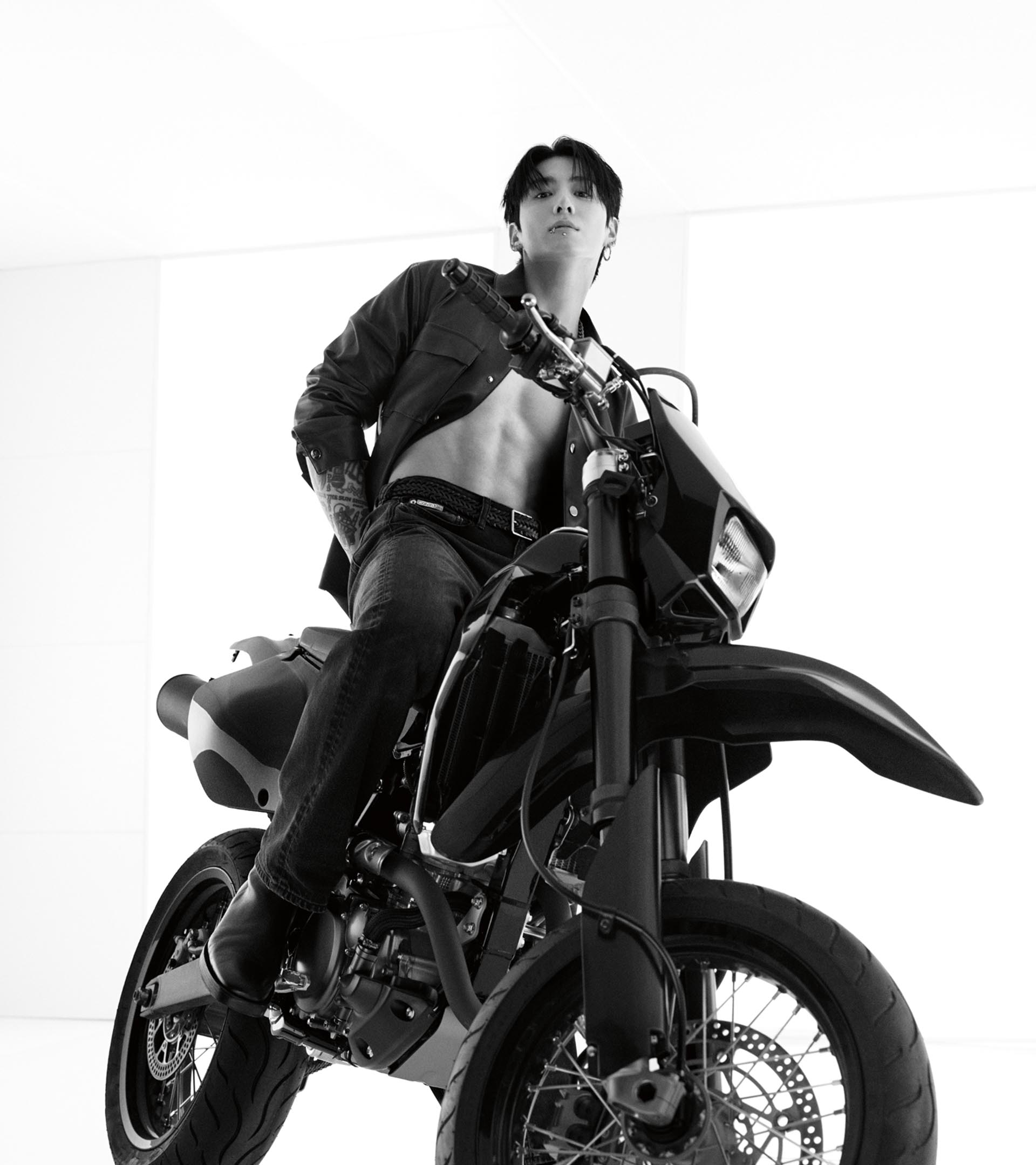 Jung Kook posing on a motorcycle in an unbuttoned oxford shirt and jeans