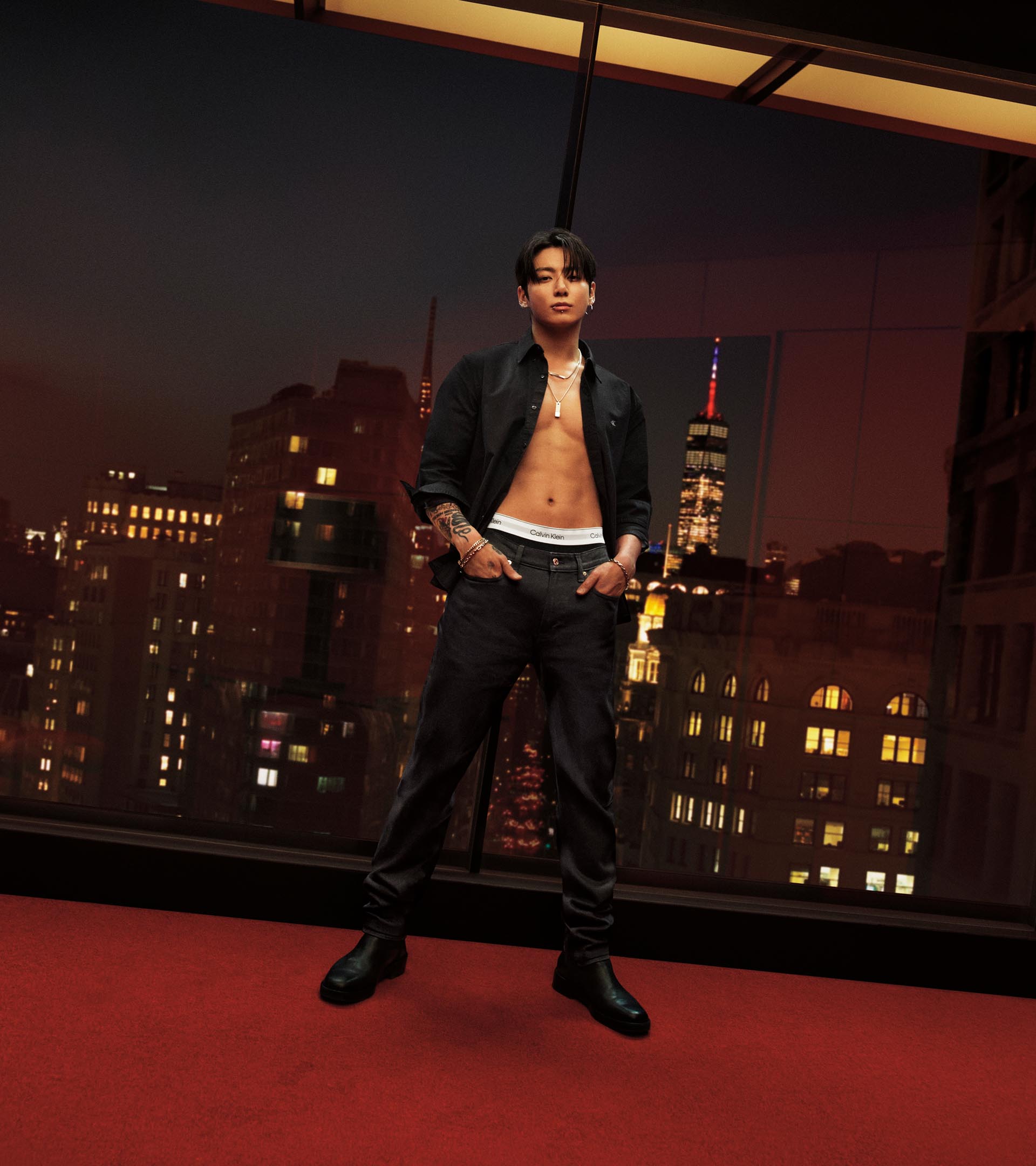 Jung Kook posing in an unbuttoned oxford shirt and jeans