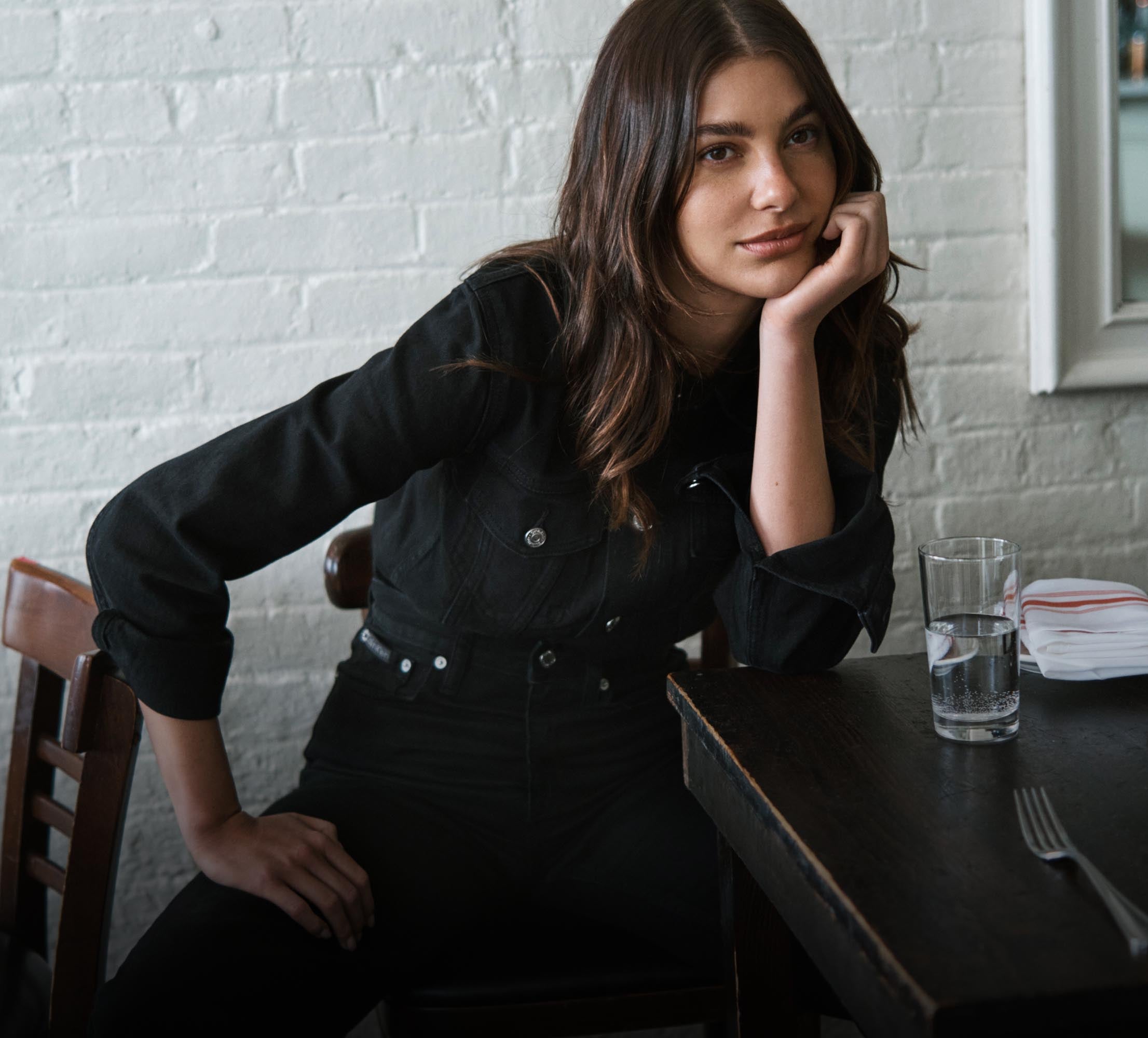 Camila Marrone leaning on a table wearing a matching dark blue denim shirt and denim jeans