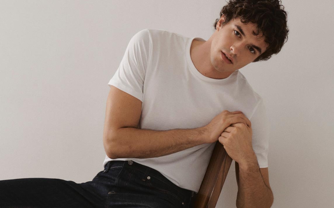 A model leaning back in his chair wearing a white t-shirt and jeans