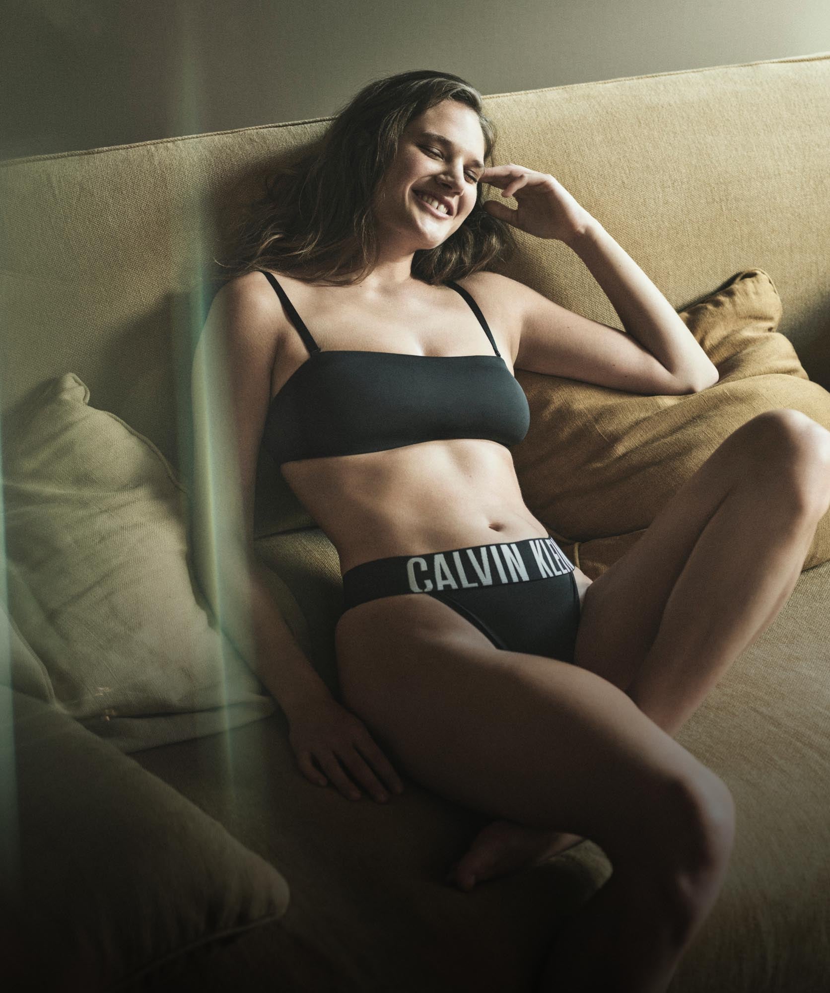 Model laying down posing wearing a matching black bralette and bikini with a Calvin Klein logo waistband