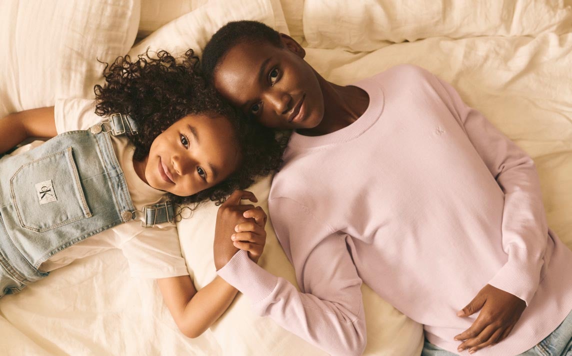 A mother and daughter posing in bed wearing Calvin Klein apparel styles