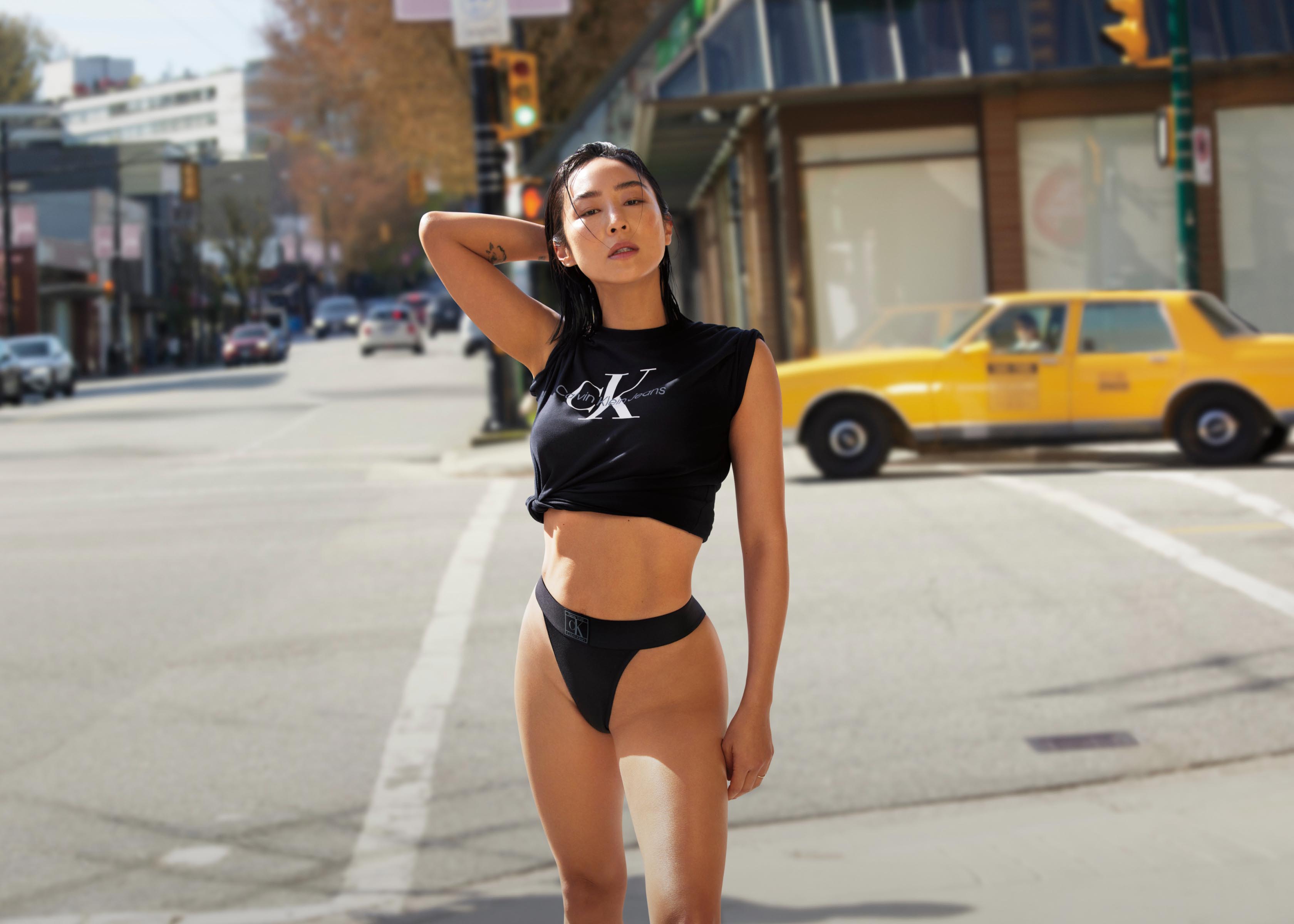 Greta Lee posing in the street wearing a black CK Monogram Logo t-shirt