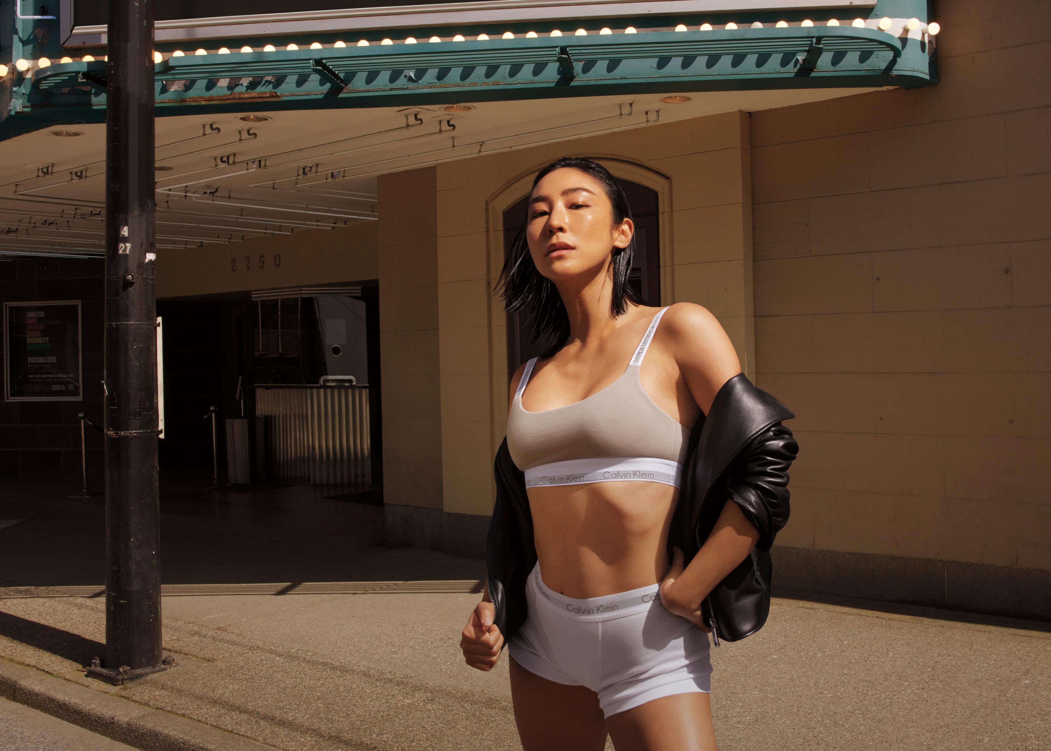 Greta Lee posing outside in grey underwear and a black leather jacket
