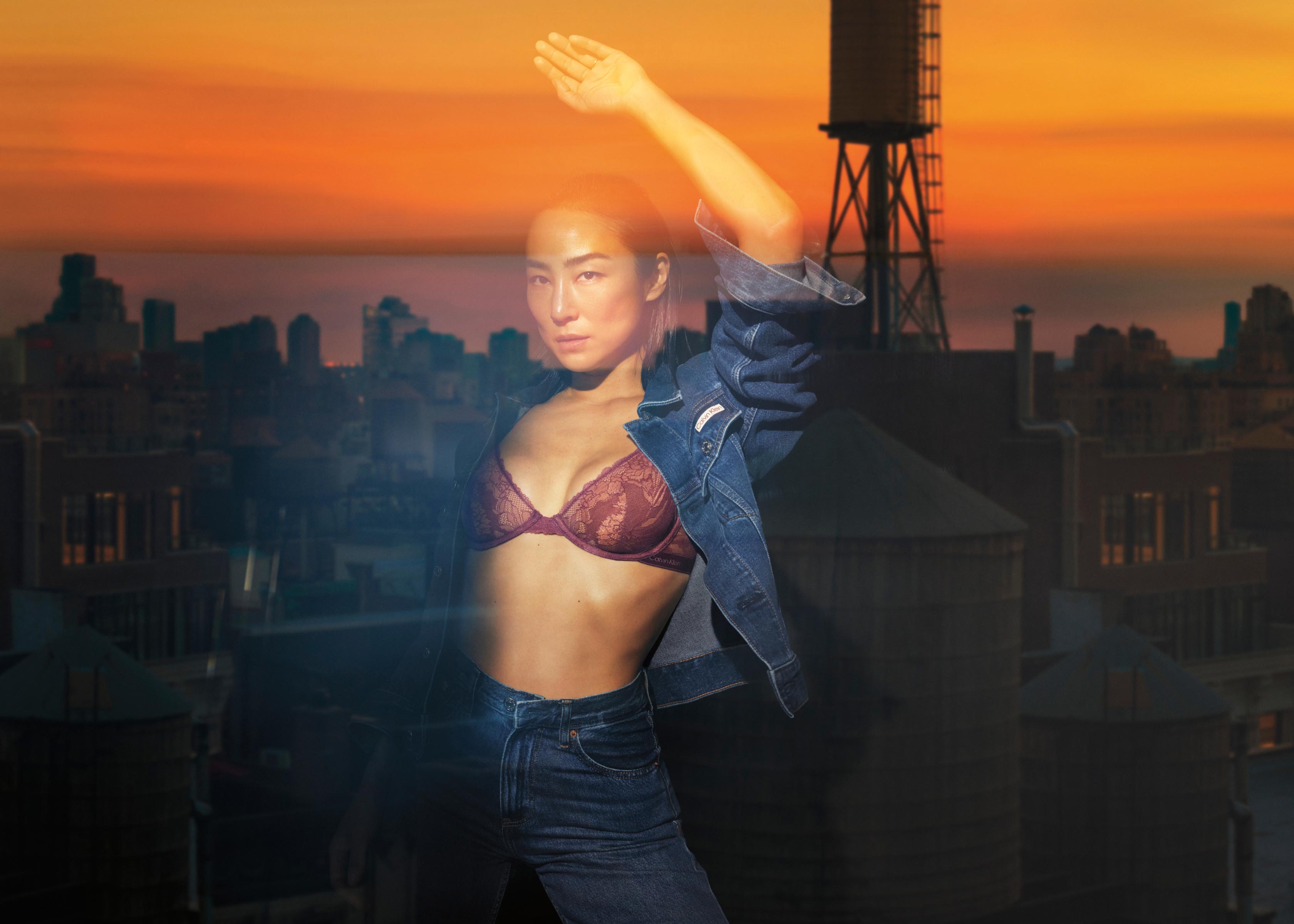 Greta Lee posing in a window wearing a dark blue denim trucker jacket