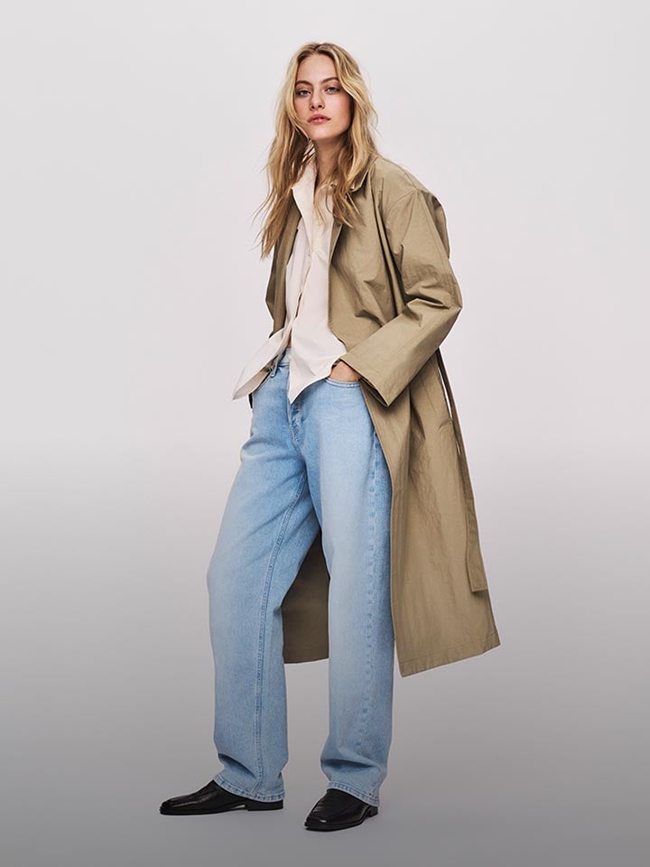 Model posing in a trench coat and white button down shirt