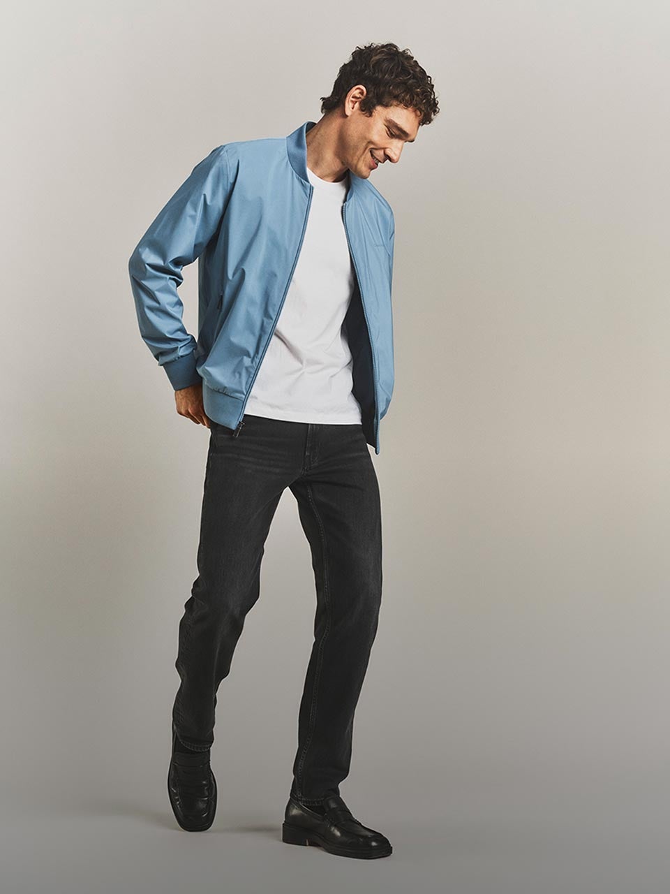 Model posing in a bomber jacket, white t-shirt, and dark denim jeans