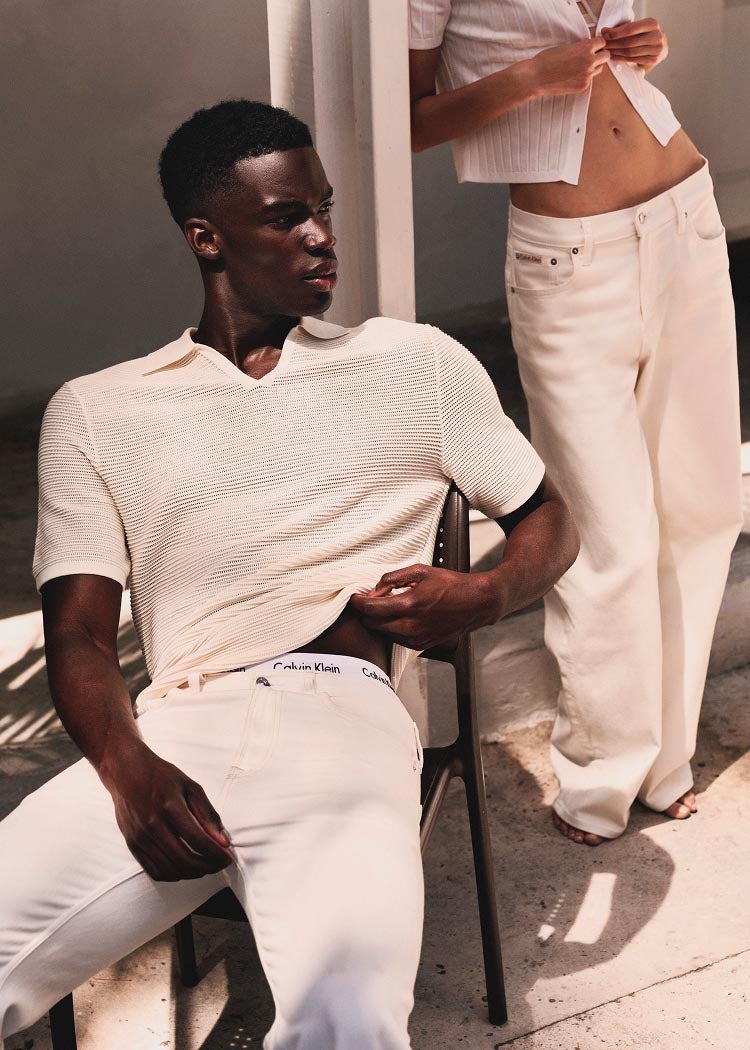 Model posing in white sweater polo and white denim.