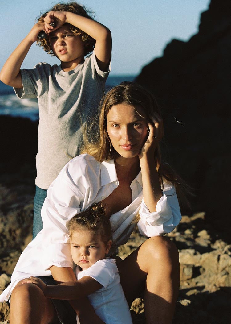Model posing in a white button down with two children on the beach.