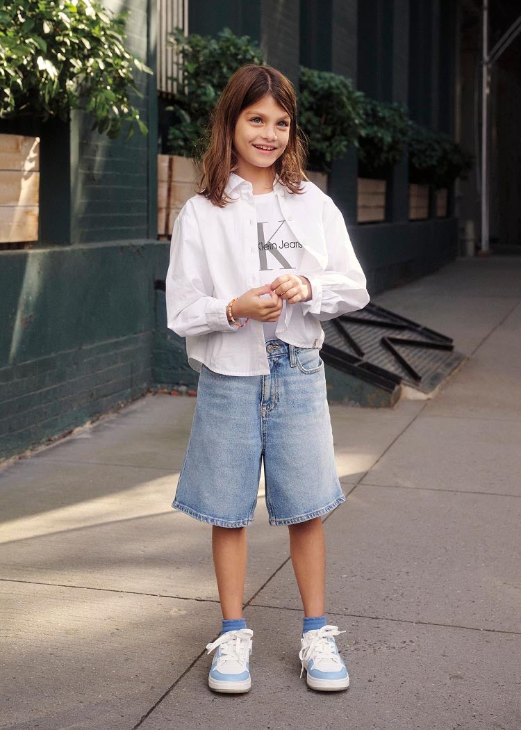 Girl posing in Calvin Klein graphic t-shirt, denim shorts and white shirt