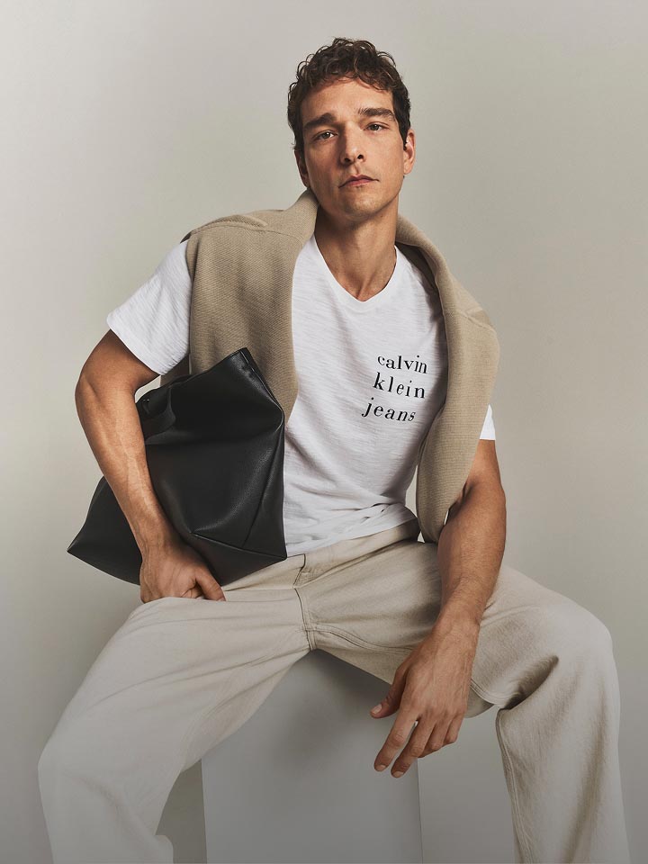 Model posing in light wash jeans and a white graphic tee.