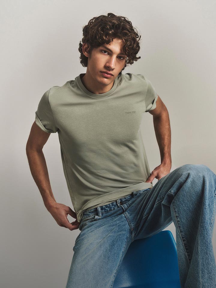 Model posing in a green t-shirt and medium wash denim jeans.
