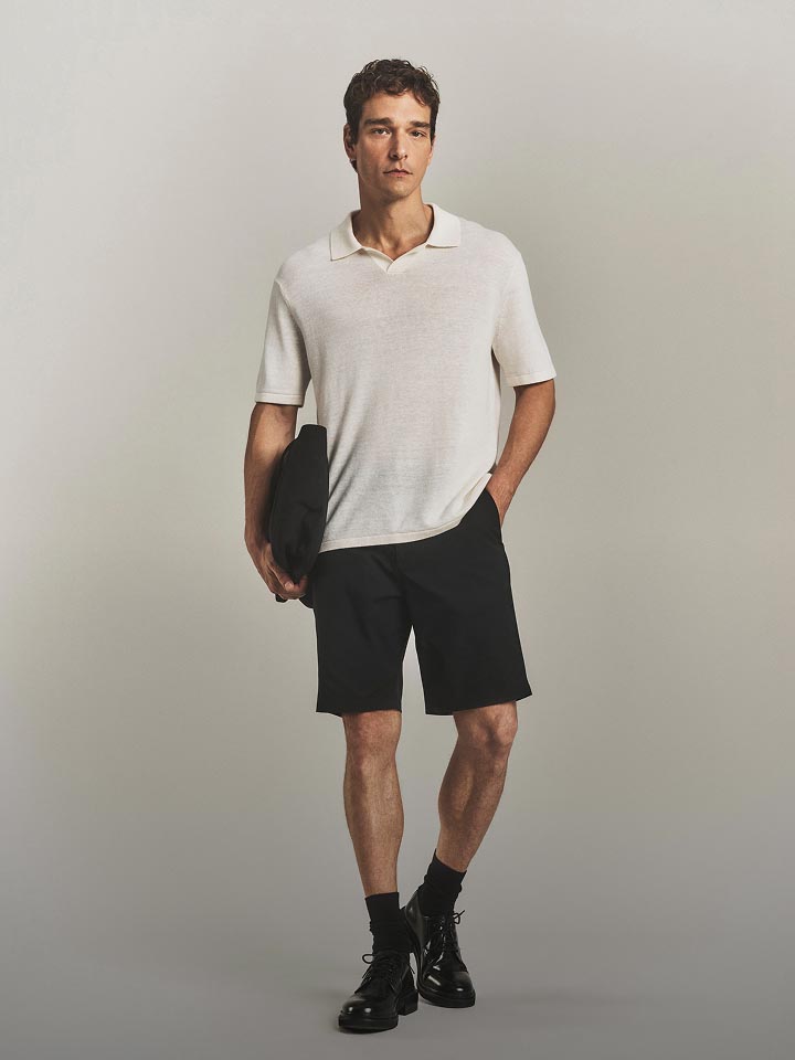 Model posing in a white lightweight sweater polo and shorts.