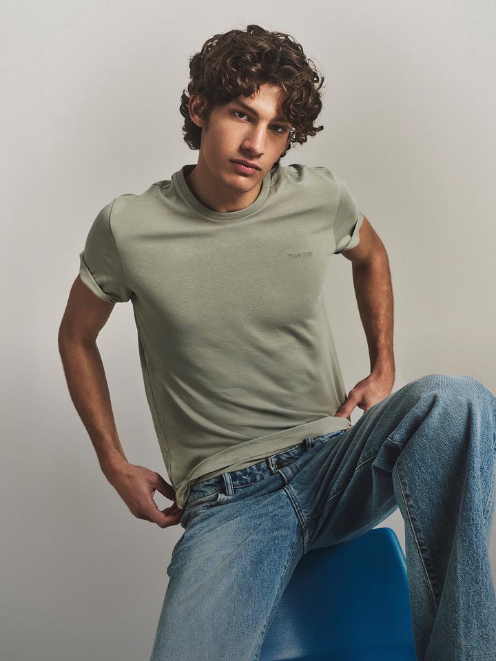 Model posing in a green t-shirt and medium wash denim jeans.