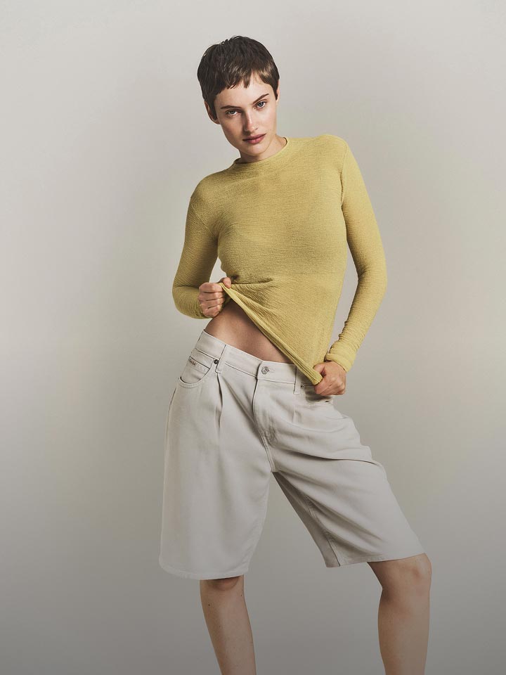 Model posing in a light yellow long sleeve sweater.