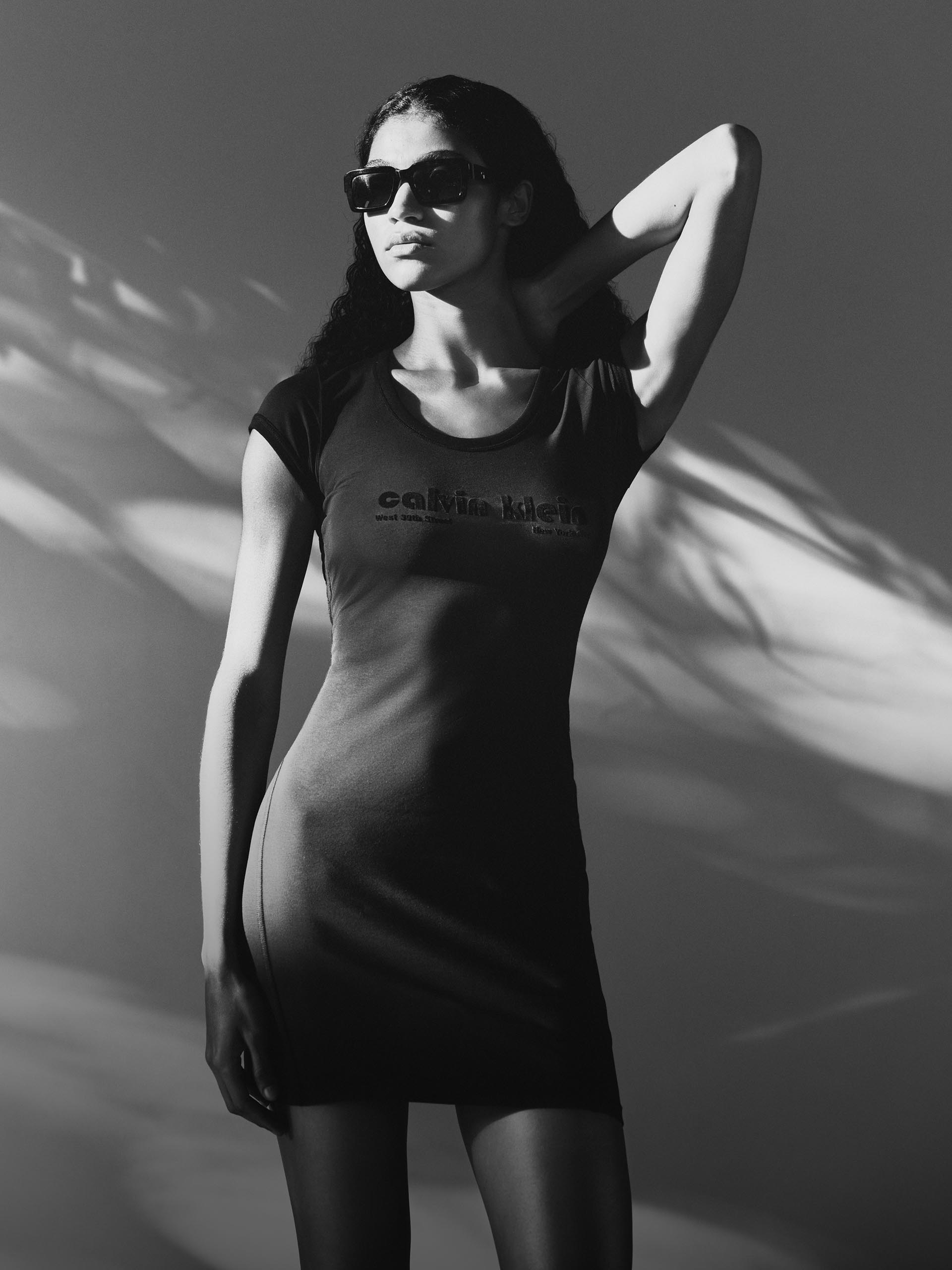 Black and white image of a model wearing a casual and laid-back t-shirt dress while wearing sunglasses.