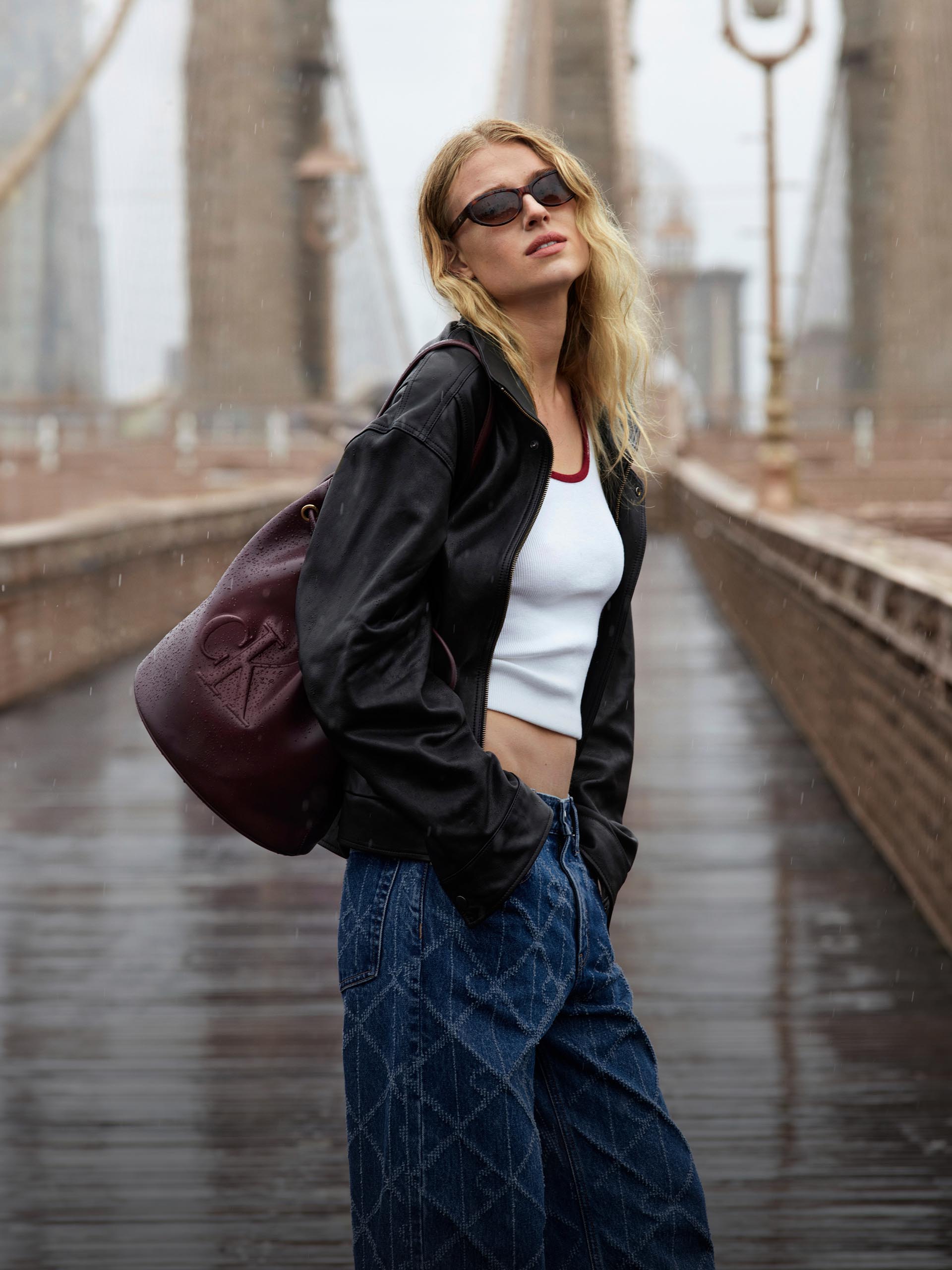 Model wearing a white tank top and black faux leather jacket on the Brooklyn Bridge.