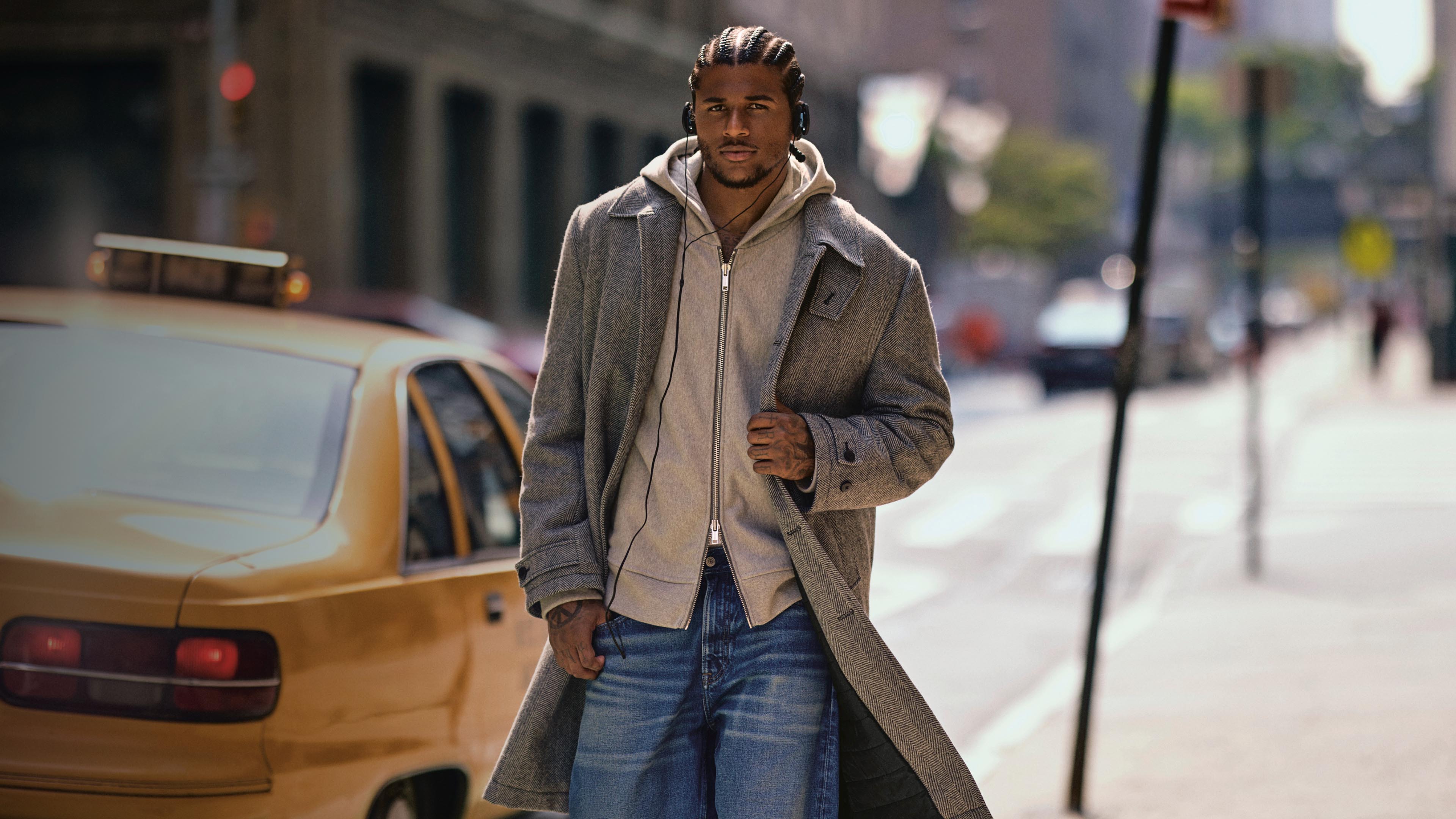 Jalen Green wearing a long wool coat while walking down the street and listening to music.