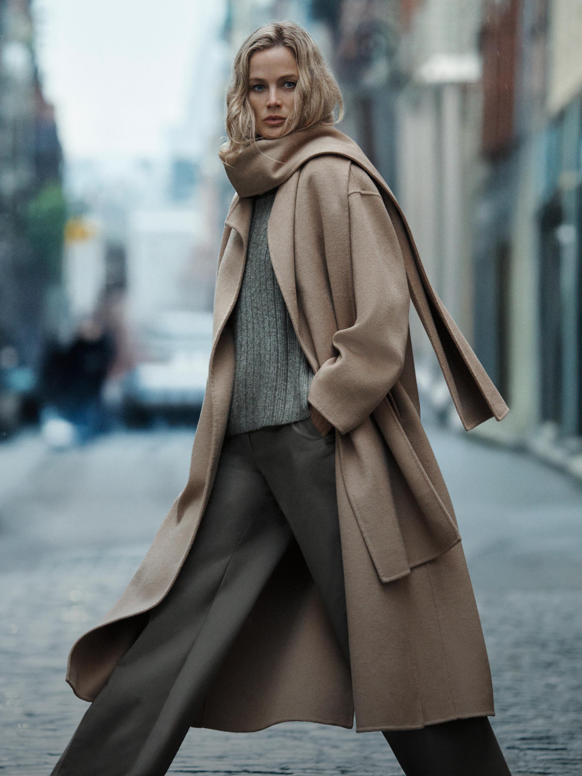 Model posing in a long tan wool coat.