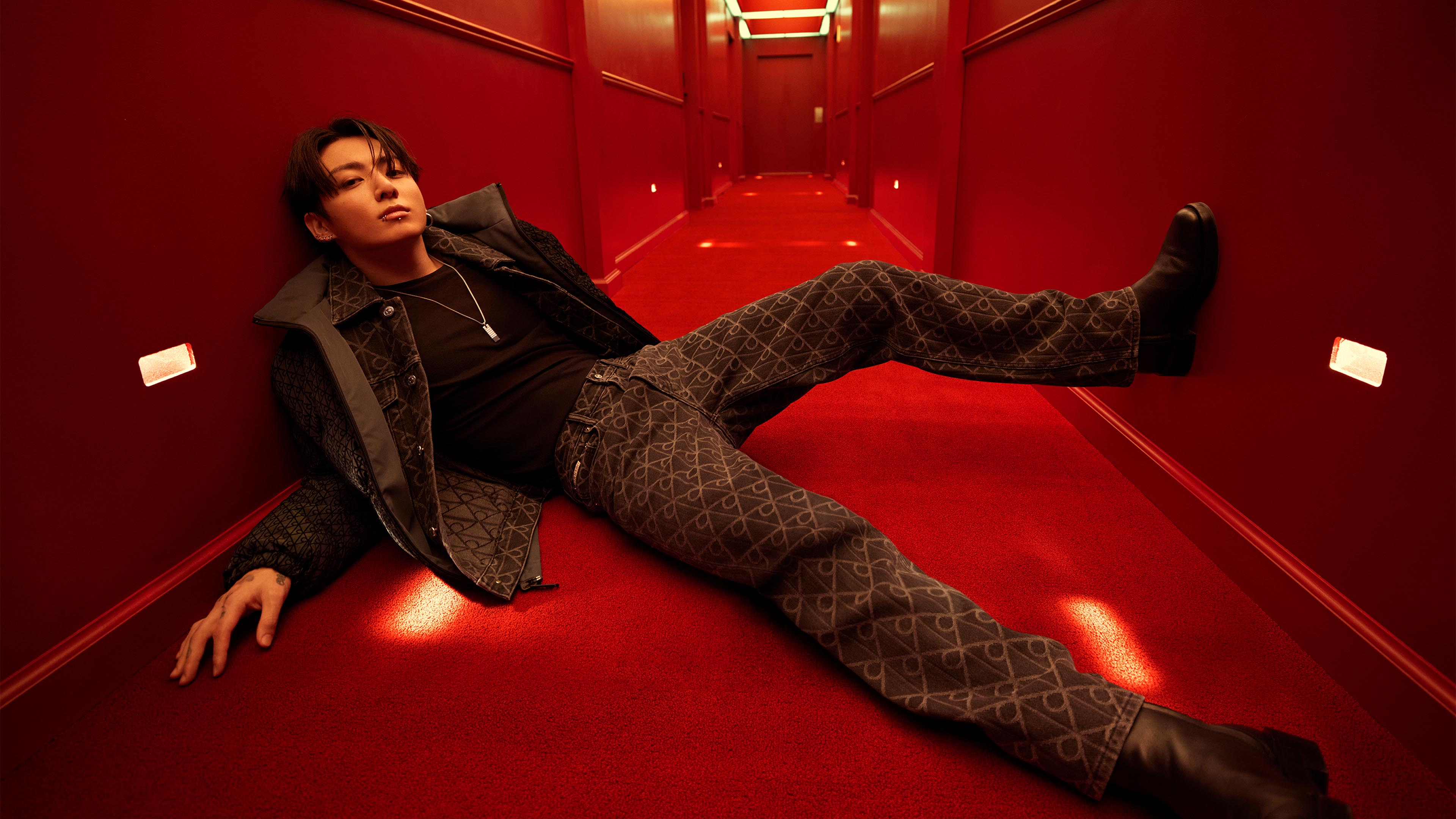 Jung Kook posing on the floor wearing CK Logo puffer and jeans