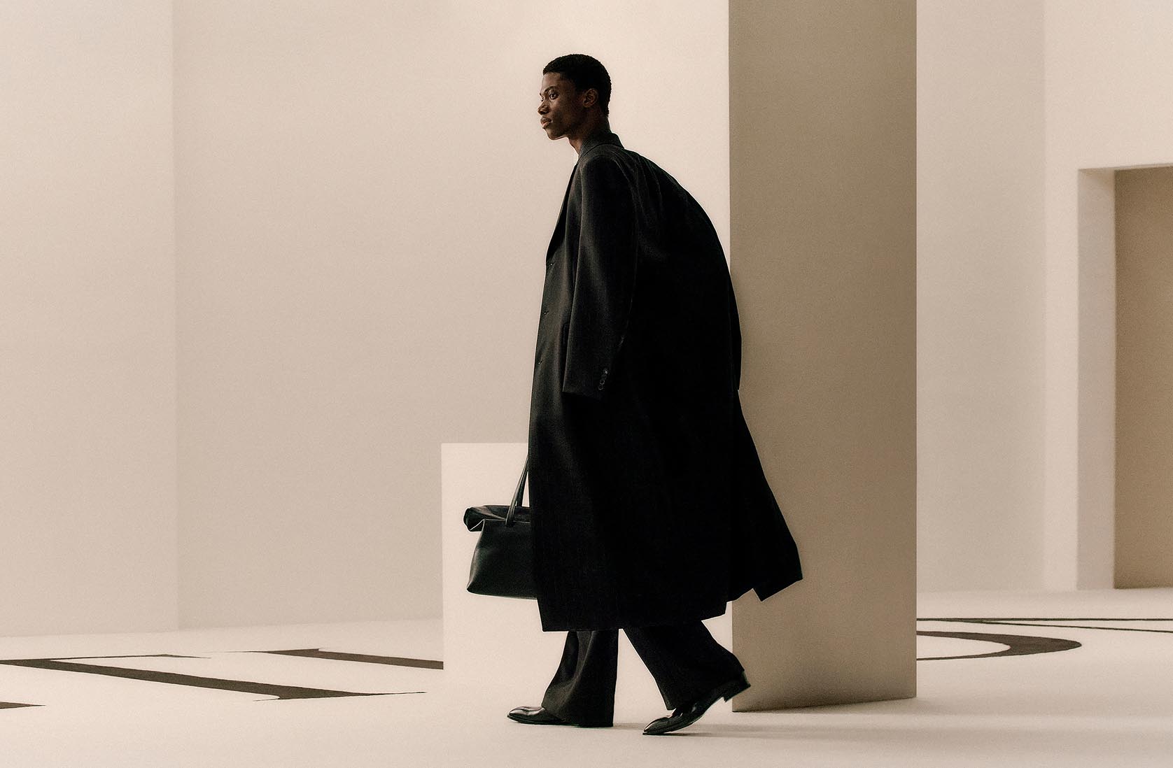 Model posing in a long black trench coat and bag