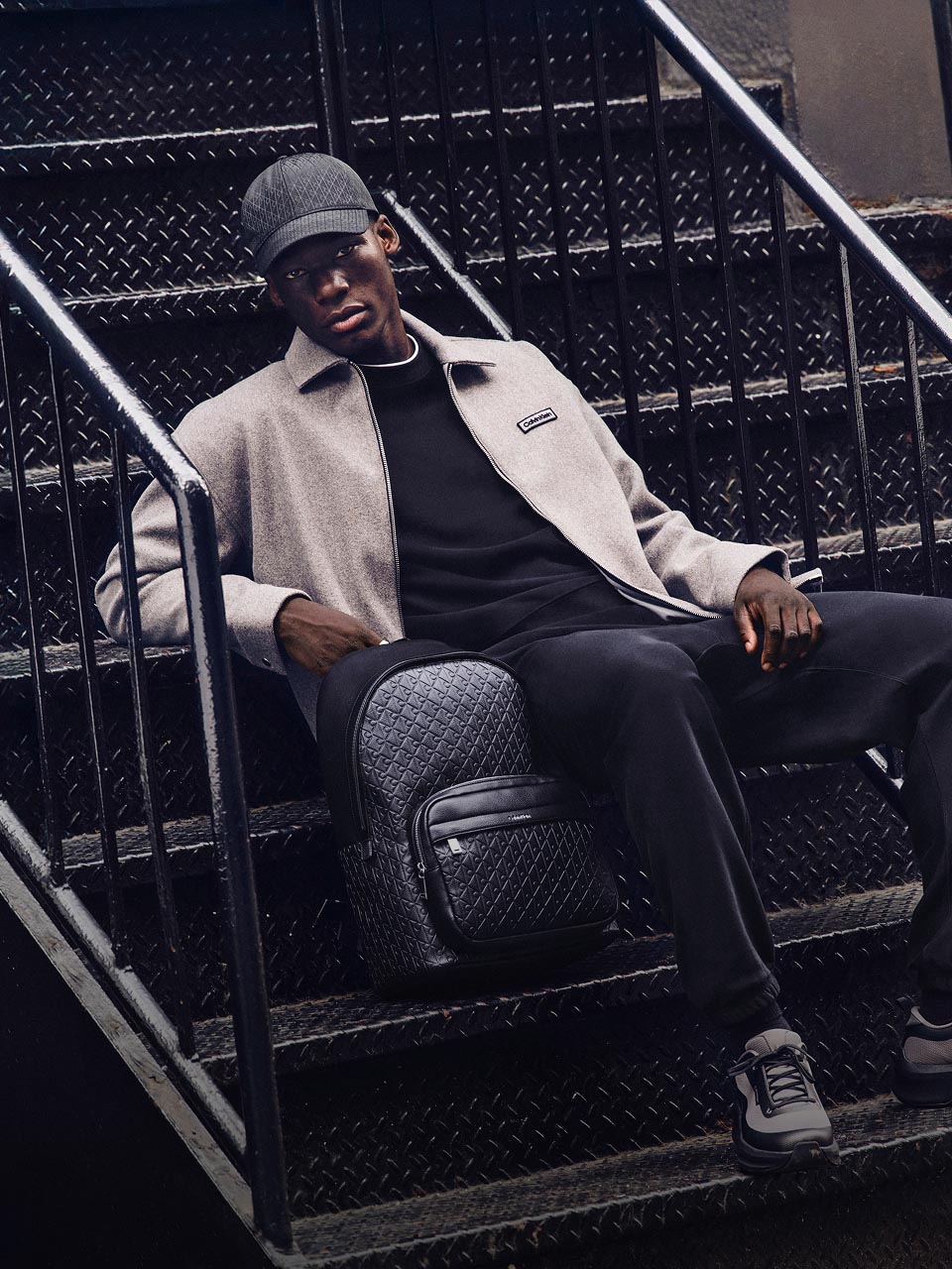 Model posing on stairs wearing a grey jacket and black pants