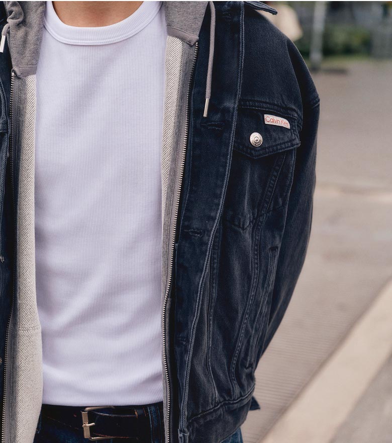 Augie posing in a denim jacket, grey hoodie, white t-shirt, and baggy jeans