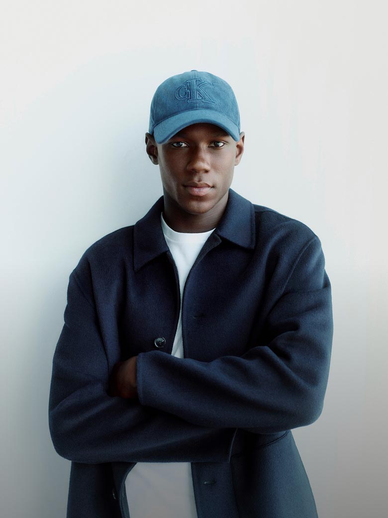 Model posing in a dark wool coat and a denim cap