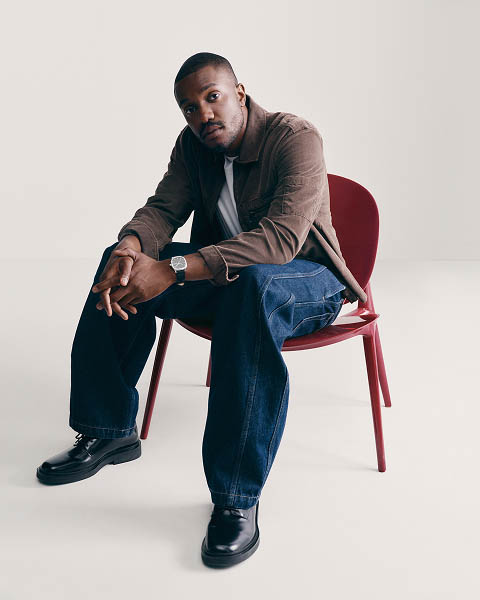 Sebastian Jean posing in a brown shirt and blue jeans