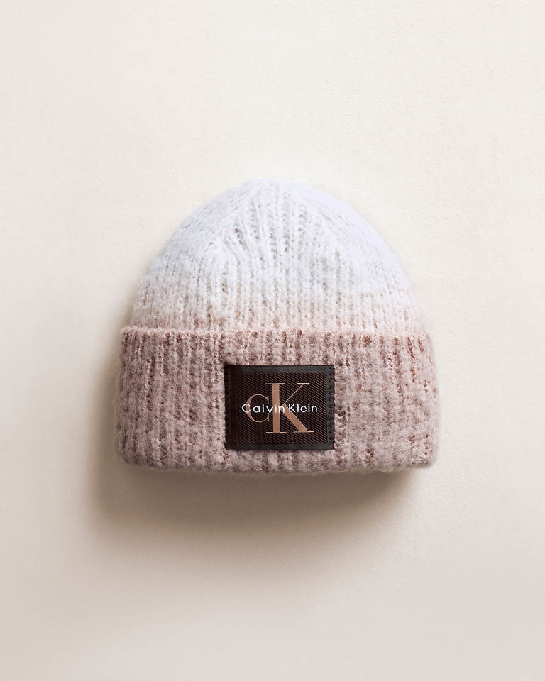 Still life image of a knitted beanie with a CK logo emblem