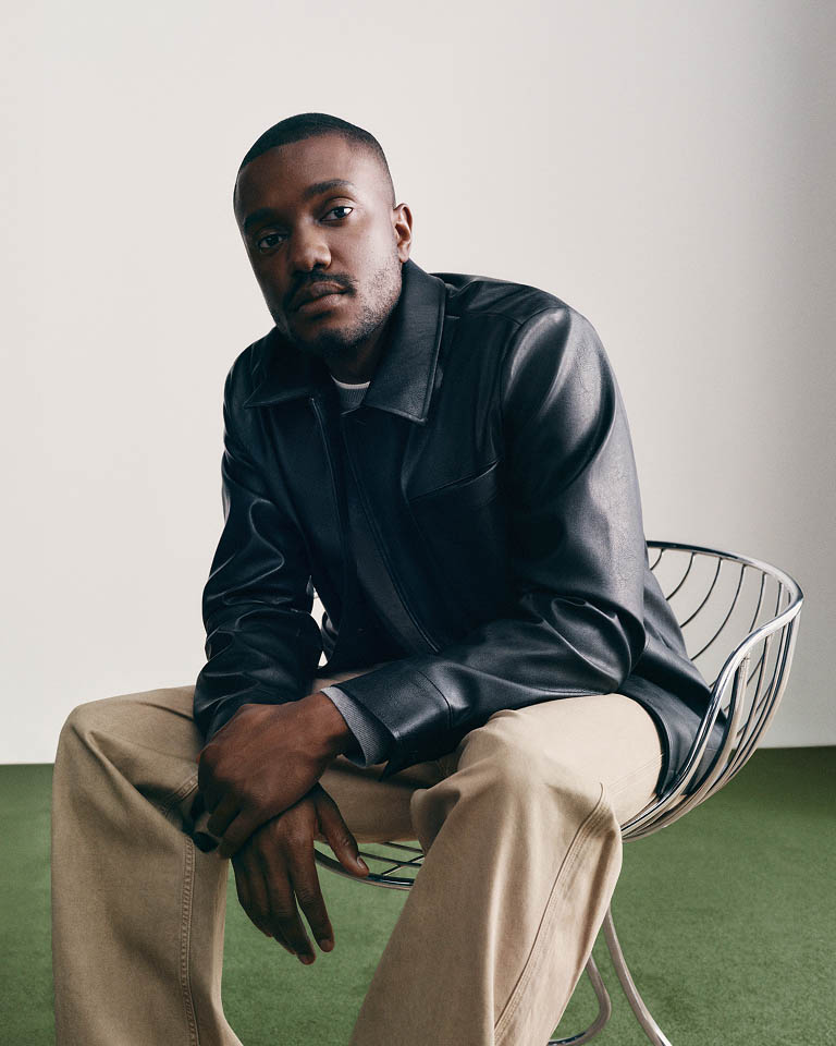Sebastian Jean posing in a leather jacket and tan pants